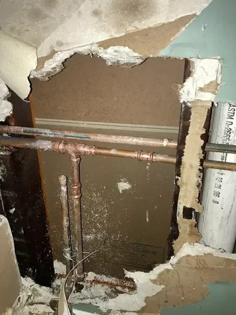 Drywall cut open so the leaking copper supply pipes can be reached and repaired