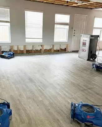 Living room with the lower drywall cut away and air movers drying the wall cavities